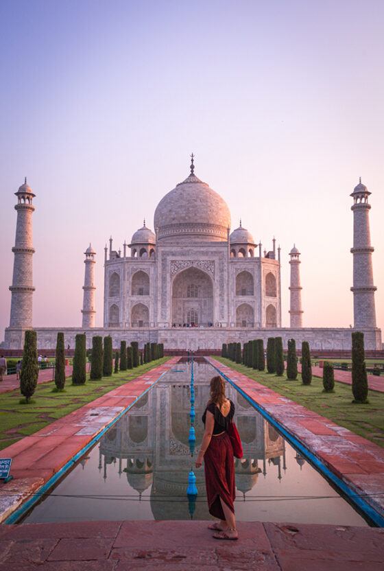 A woman standing in front of the Taj Mahal in India during sunrise.