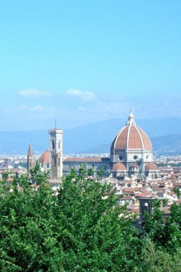 View of the Duomo in Florence from Piazzale Michelangelo with green trees in the foreground.