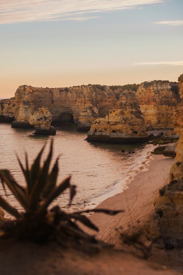 A sunset view of the iconic cliffs of Algarve, Portugal surrounded by the Pacific Ocean and an empty sandy beach down below.