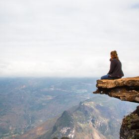 A solo woman overlooking the landscape in Vietnam while sitting on a rock.